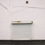 Зачинені металеві ролети у глухій білій стіні: двері, зачинені за замовчуванням
