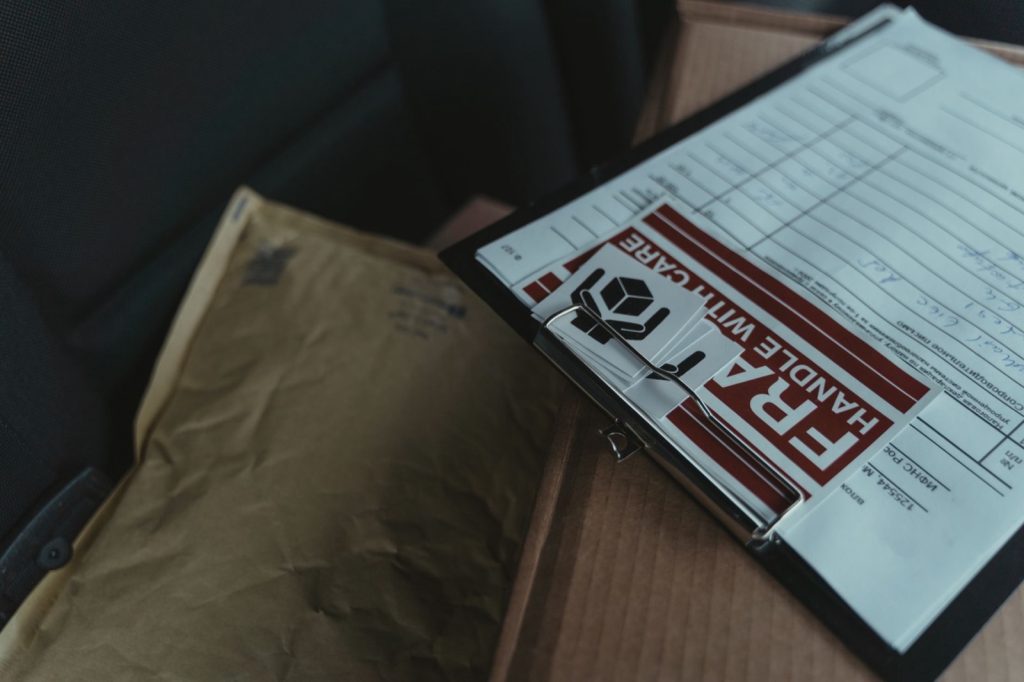 A clipboard holding a shipping form and a fragile label resting on parcels in the back of a delivery van
