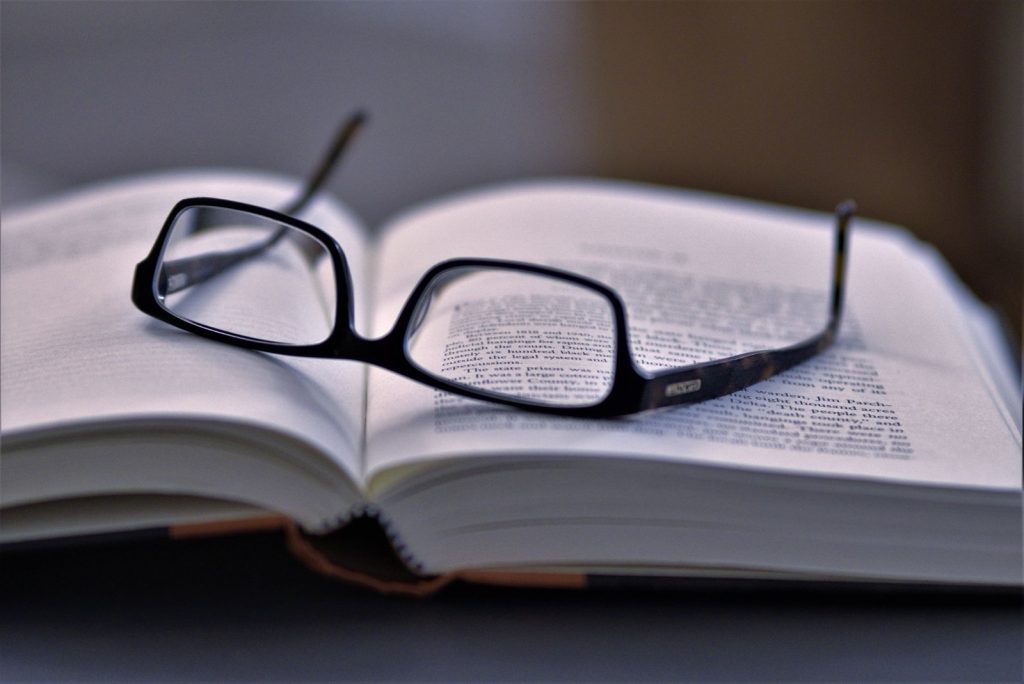 Black-framed reading glasses resting on the open pages of a densely printed book