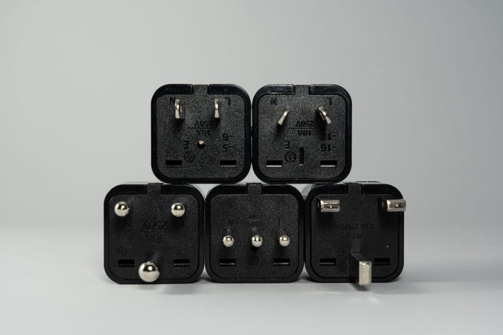 Five black international power plug adapters stacked in a pyramid on a plain background, each with a different pin pattern