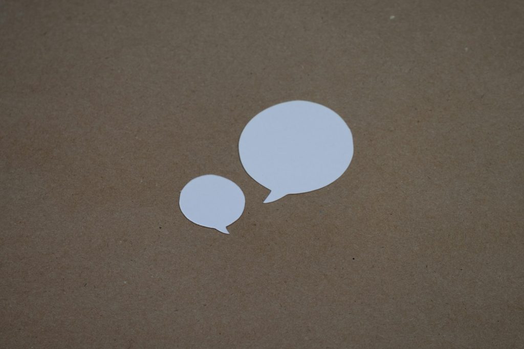 Two white paper speech bubbles of different sizes on a brown card background