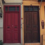 Two adjacent front doors on a street, one dark red and one brown, set into differently coloured house facades