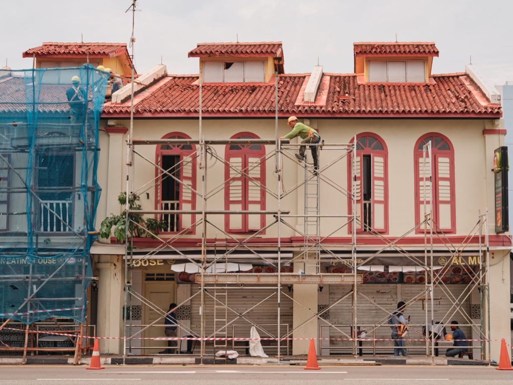 Workers on scaffolding renovating the facade of a two-storey shophouse with a red tiled roof